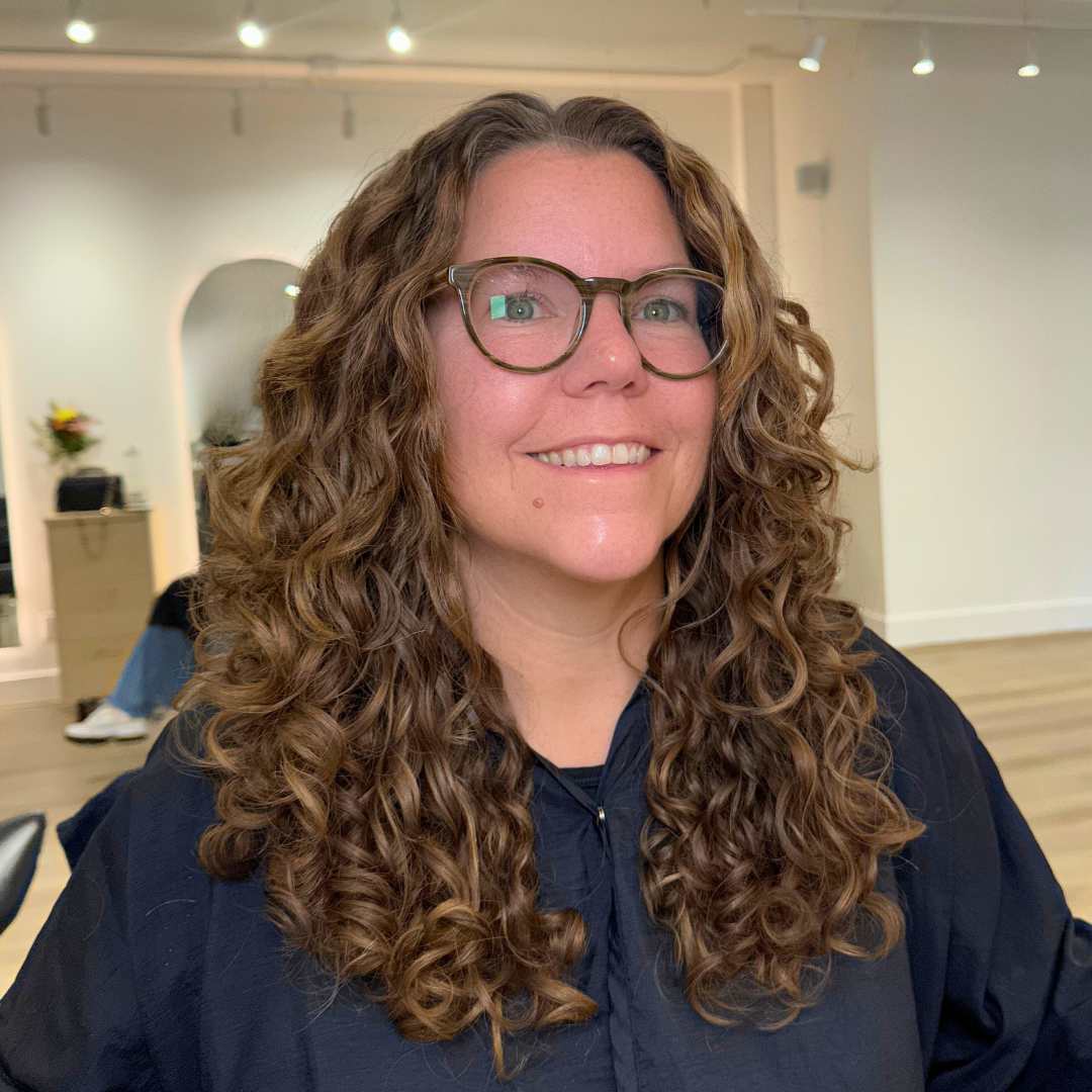 A woman with brown hair sits in a curly hair salon located in vancouver, having a curly hair cut