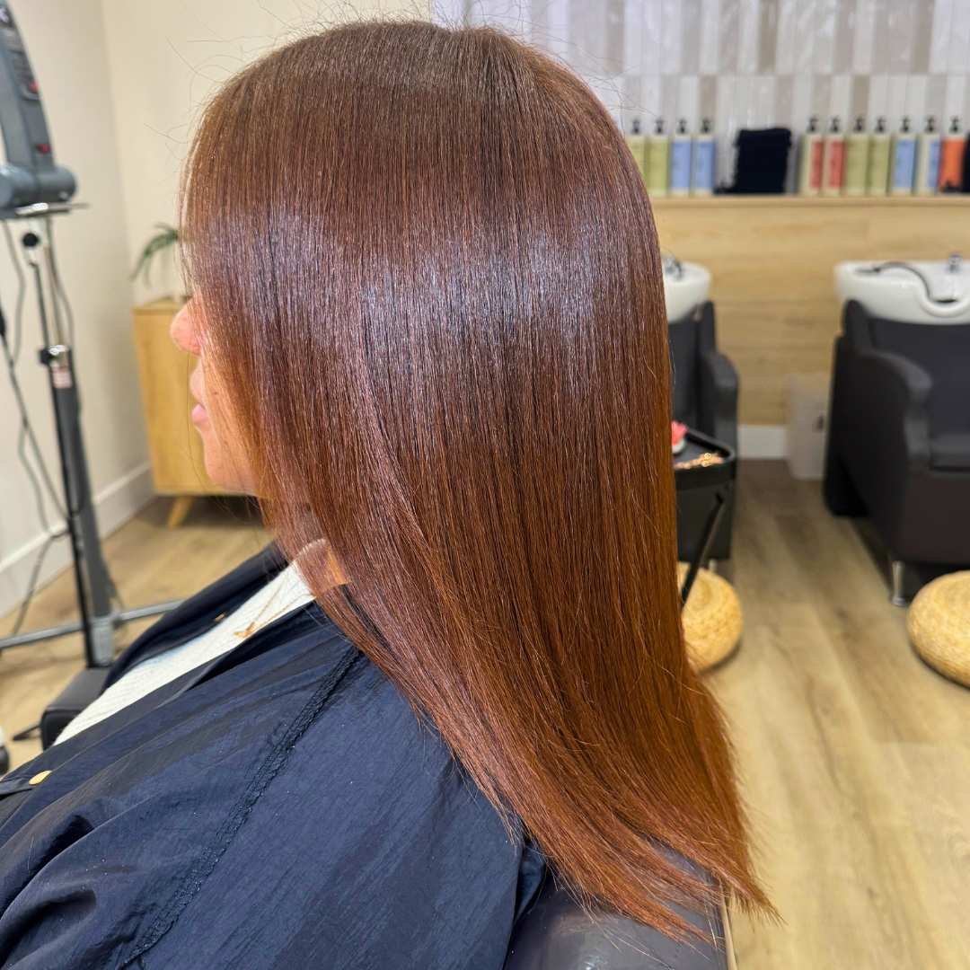 A woman with long brown hair sits in a salon, focusing on restoring damaged hair and promoting healthy growth.
