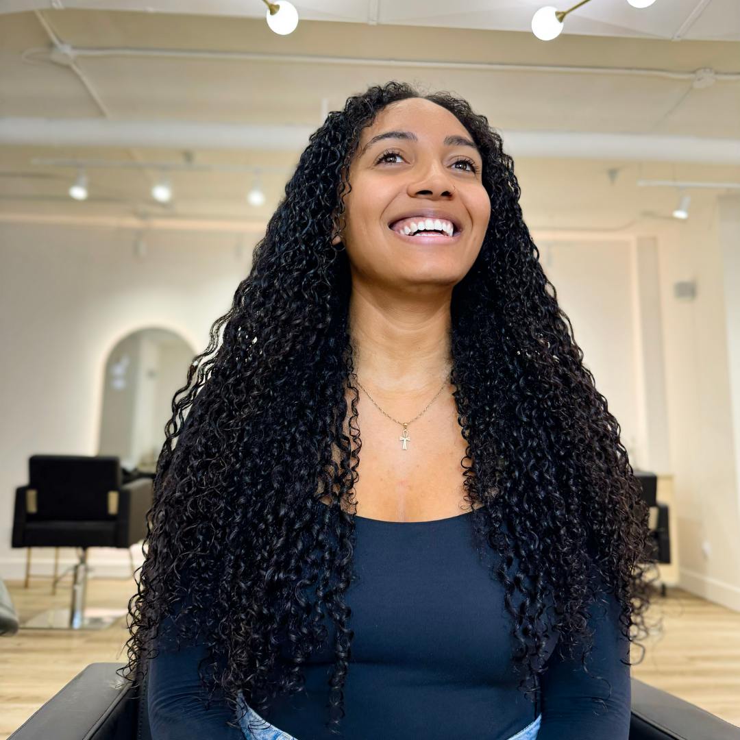 A woman with long Curly hair sits in a salon, focusing on scalp care