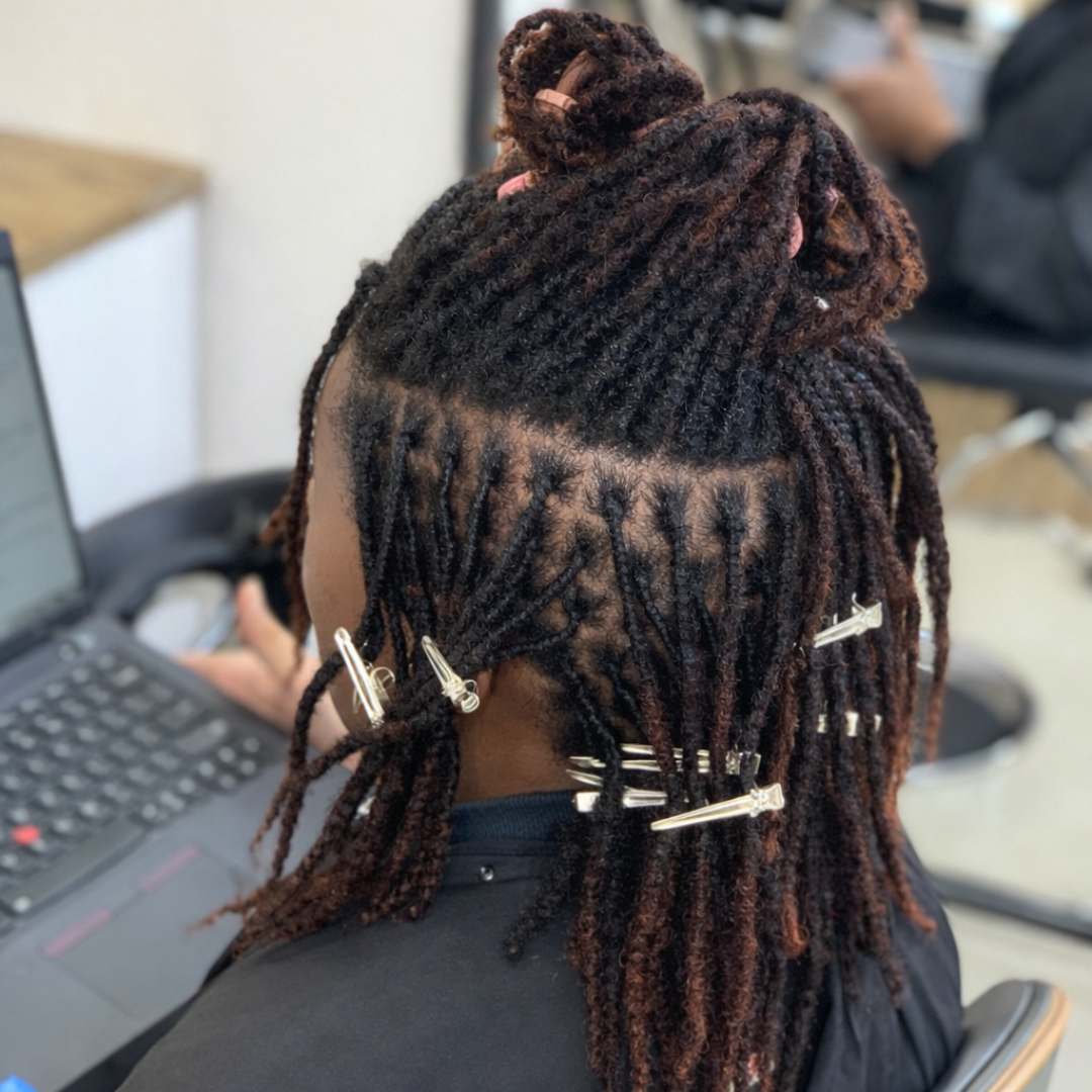 Back view of long brown locs in a half-up style being sectioned during a loc maintenance appointment at DES Curl Spa