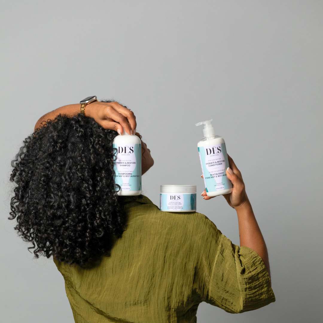 A woman with curly hair holds two bottles of hair care products, including the Volume EdgeLift Brush, smiling confidently.